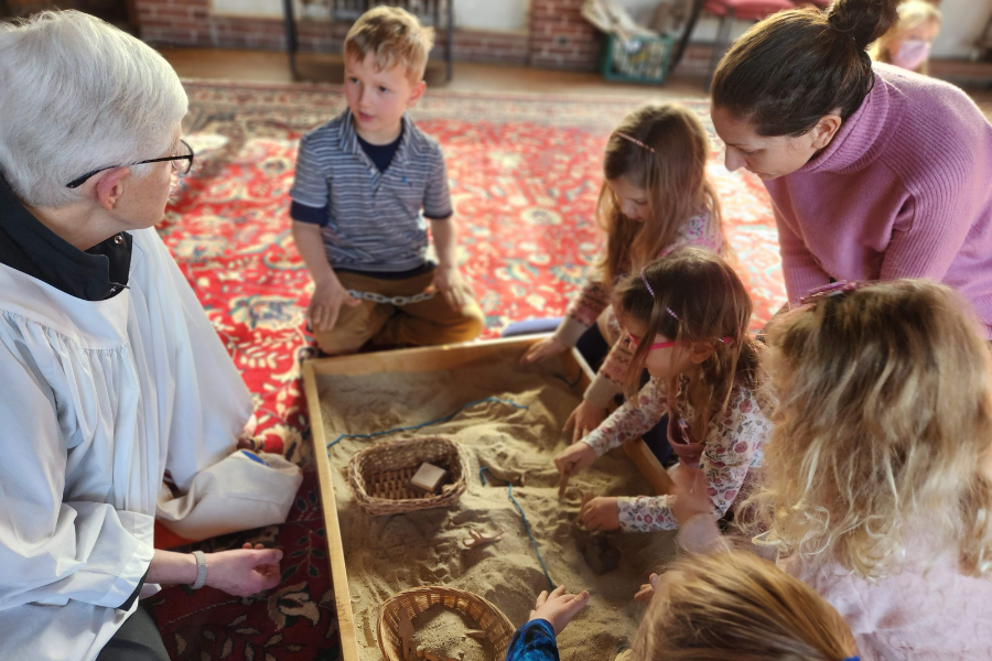 Adult leaders and children around a sandbox during a Godly Play class at Parish of the Epiphany, Winchester