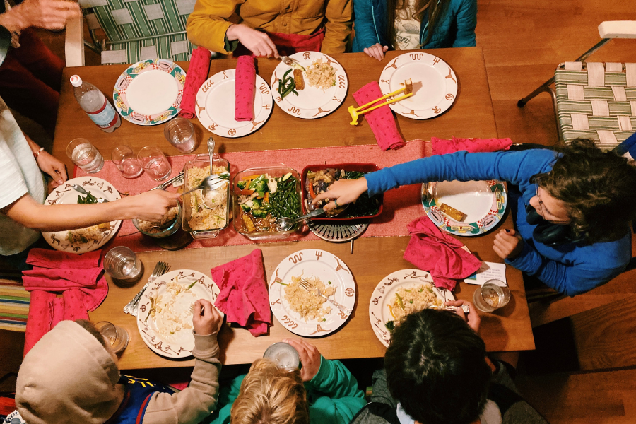 Photo taken from above of youth seated around dining table sharing a meal
